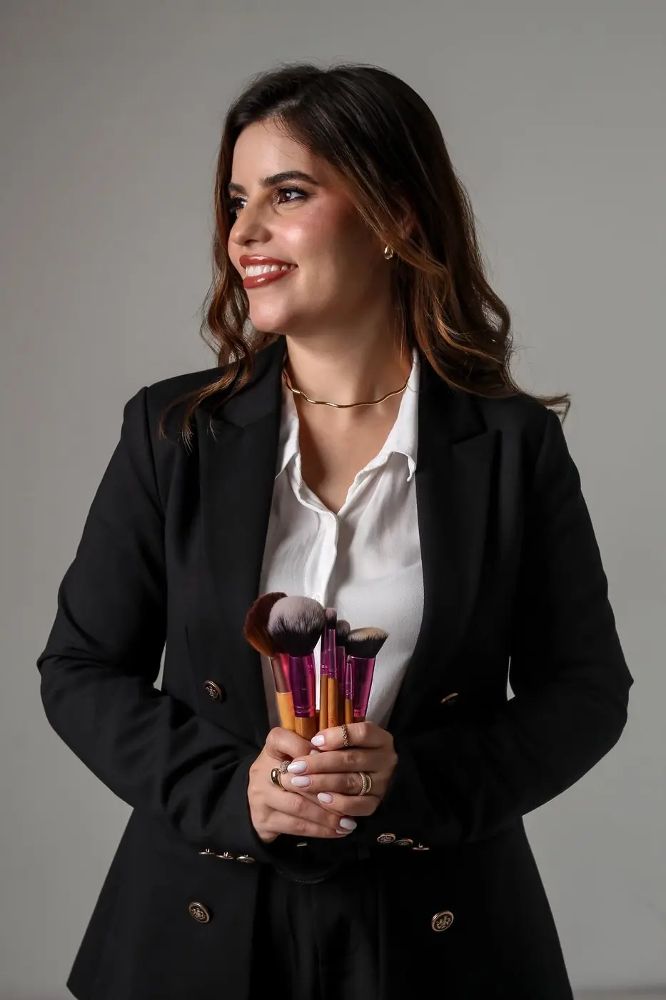 Alessandra Rodrigues de blazer preto segurando pincéis de maquiagem