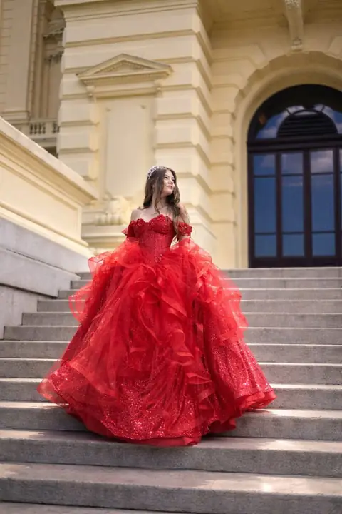 Debutante de vestido vermelho com babados sentada na escadaria de um prédio histórico