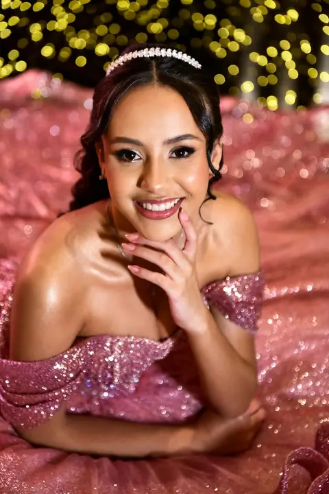 Debutante sorrindo com tiara e vestido rosa de brilho, maquiagem iluminada