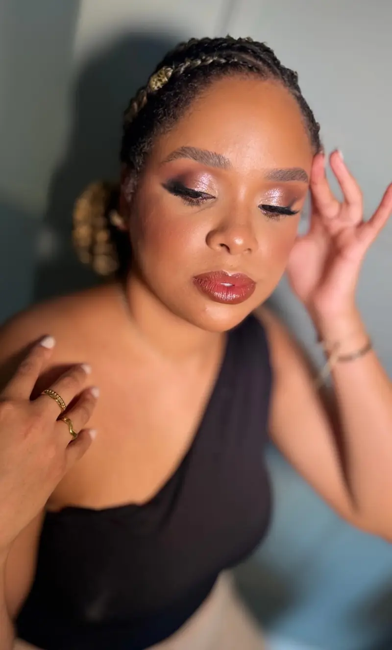 Mulher de tranças com maquiagem de olhos esfumados em tons de bronze e batom marrom brilhante