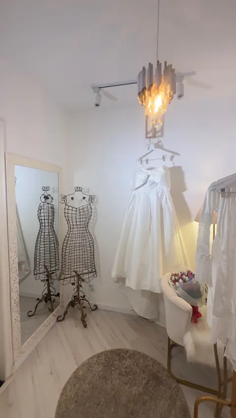 Provador com vestido de noiva pendurado sob o lustre, manequins de arame dourado e espelho
