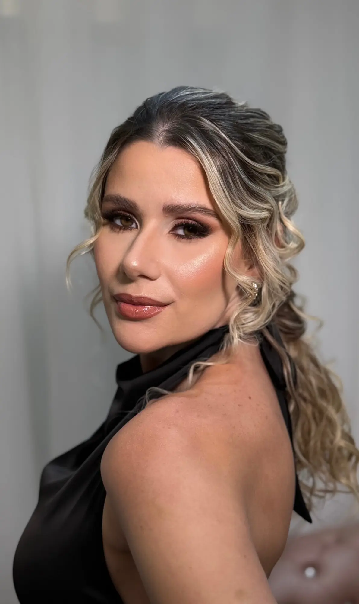 Cliente loira de cabelo semipreso ondulado, blusa preta de gola alta e esfumado marrom