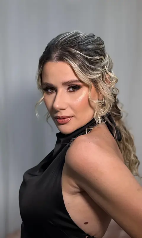 Mulher loira de perfil com vestido preto, maquiagem esfumada e penteado semipreso em ondas