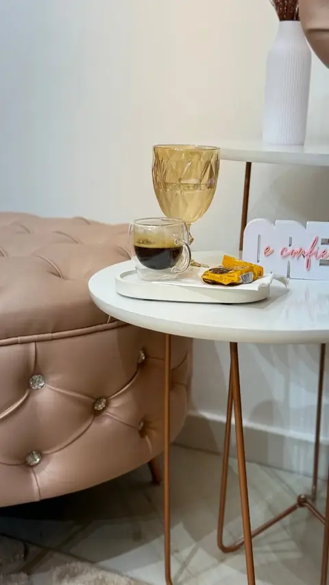 Mesa de apoio com café e taça dourada ao lado de um puff capitonê no espaço AR Concept