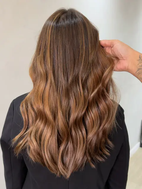 Cabelo castanho com luzes caramelo em ondas, visto de costas