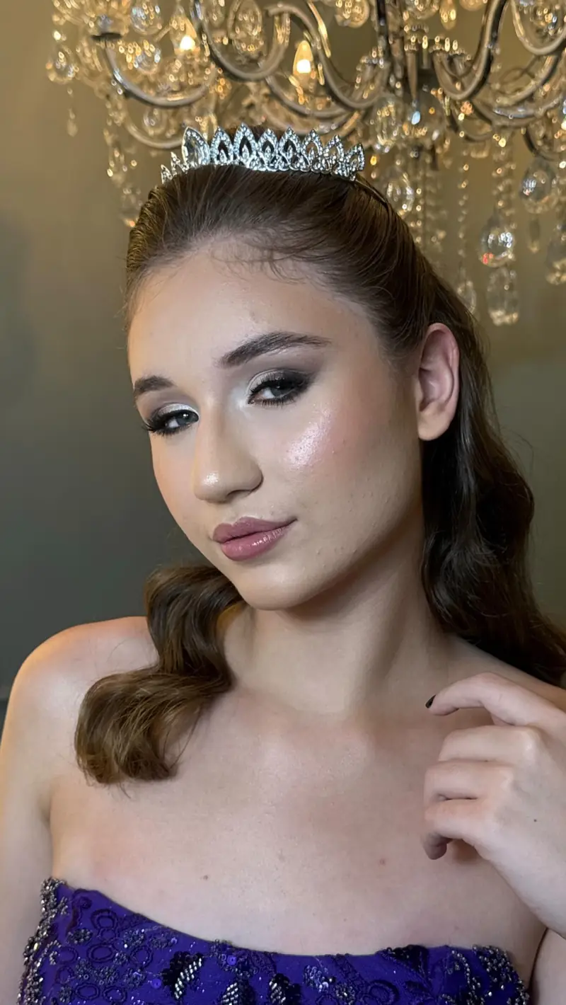 Debutante de tiara e vestido roxo bordado, cabelo solto em ondas, sob um lustre de cristal