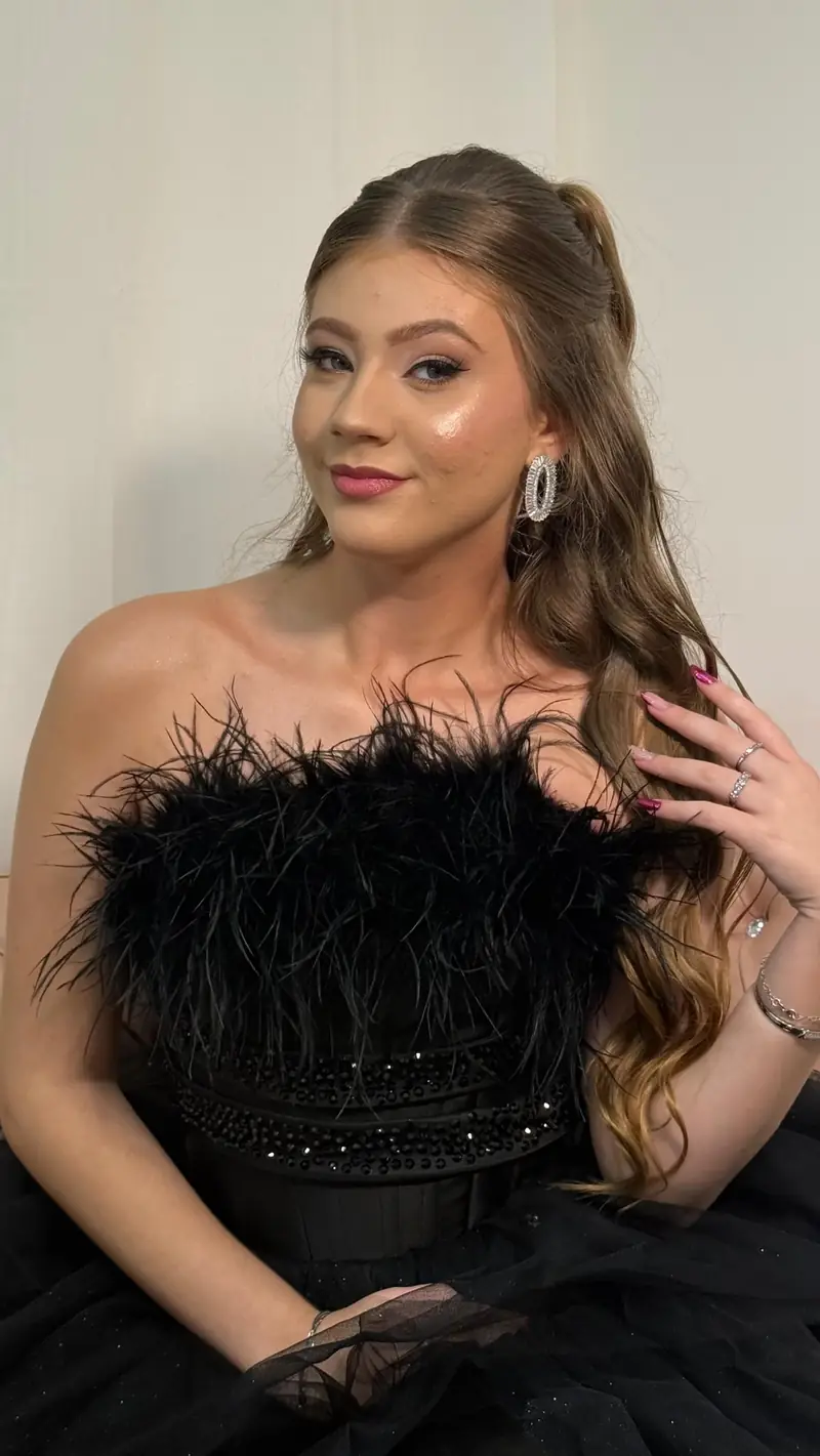 Debutante de vestido preto com plumas, cabelo semipreso ondulado e brincos grandes