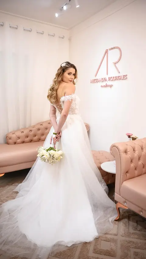 Noiva de costas olhando por cima do ombro, com vestido de tule e cabelo solto ondulado, no lounge rosa do espaço AR Concept