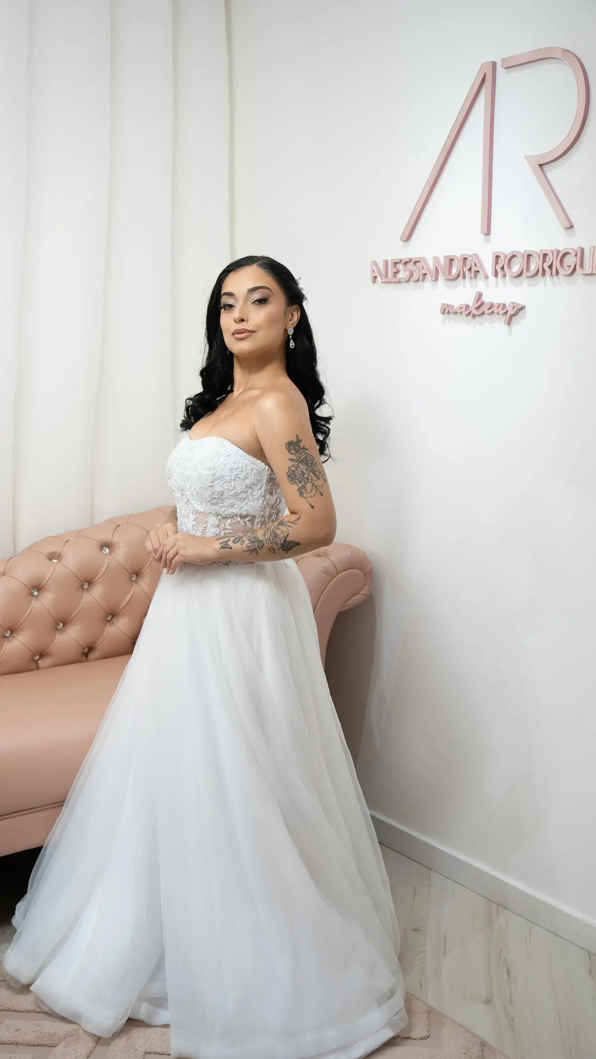 Noiva morena de cabelo solto e vestido tomara que caia, encostada no sofá capitonê rosa do espaço AR Concept
