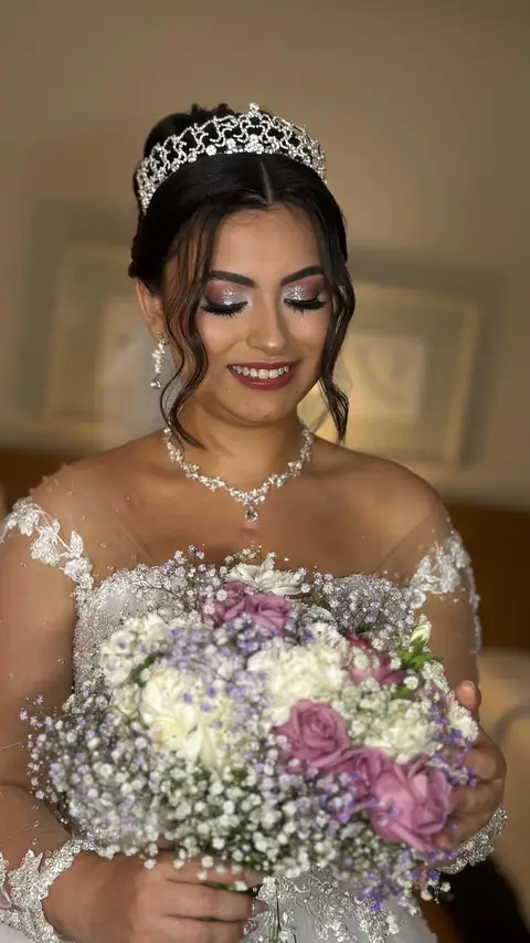 Noiva sorrindo com tiara, colar e buquê lilás e rosa com mosquitinho