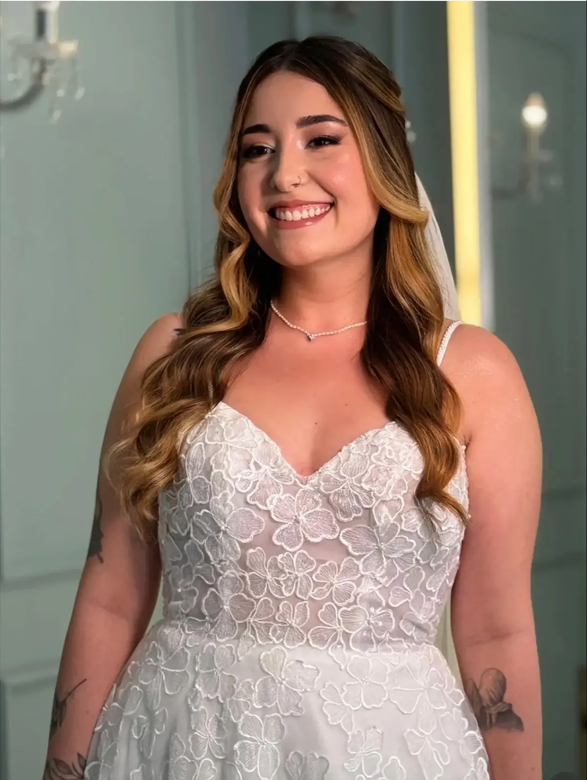 Noiva sorrindo, de cabelo solto ondulado e vestido de renda floral