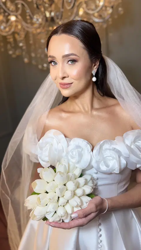 Noiva com cabelo preso liso e véu, vestido com flores nos ombros e buquê de tulipas brancas