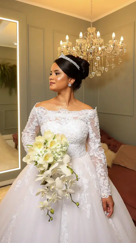 Noiva de perfil com coque e tiara, vestido de renda com manga e buquê cascata de orquídeas