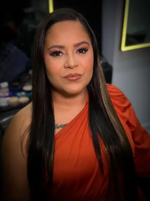 Mulher de cabelo liso longo com esfumado cobre e vestido laranja, em fundo escuro