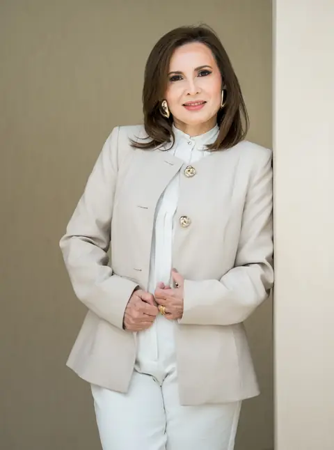 Mulher de blazer bege e camisa branca com maquiagem natural, em ensaio corporativo